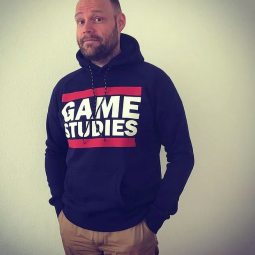 Dr. Rudolf Inderst trägt eine Hoodie mit dem Text "Game Studies" an der Vorderseite. 